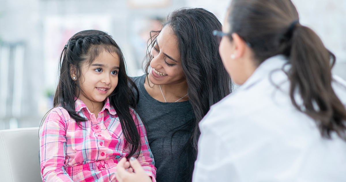 A young pre-adolescent girl sitting next to her mother while engaging with a medical provider.