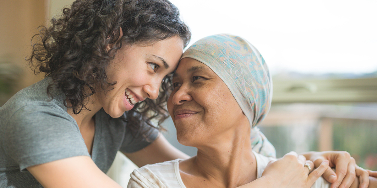 A woman wearing a head covering is embraced by a younger woman.