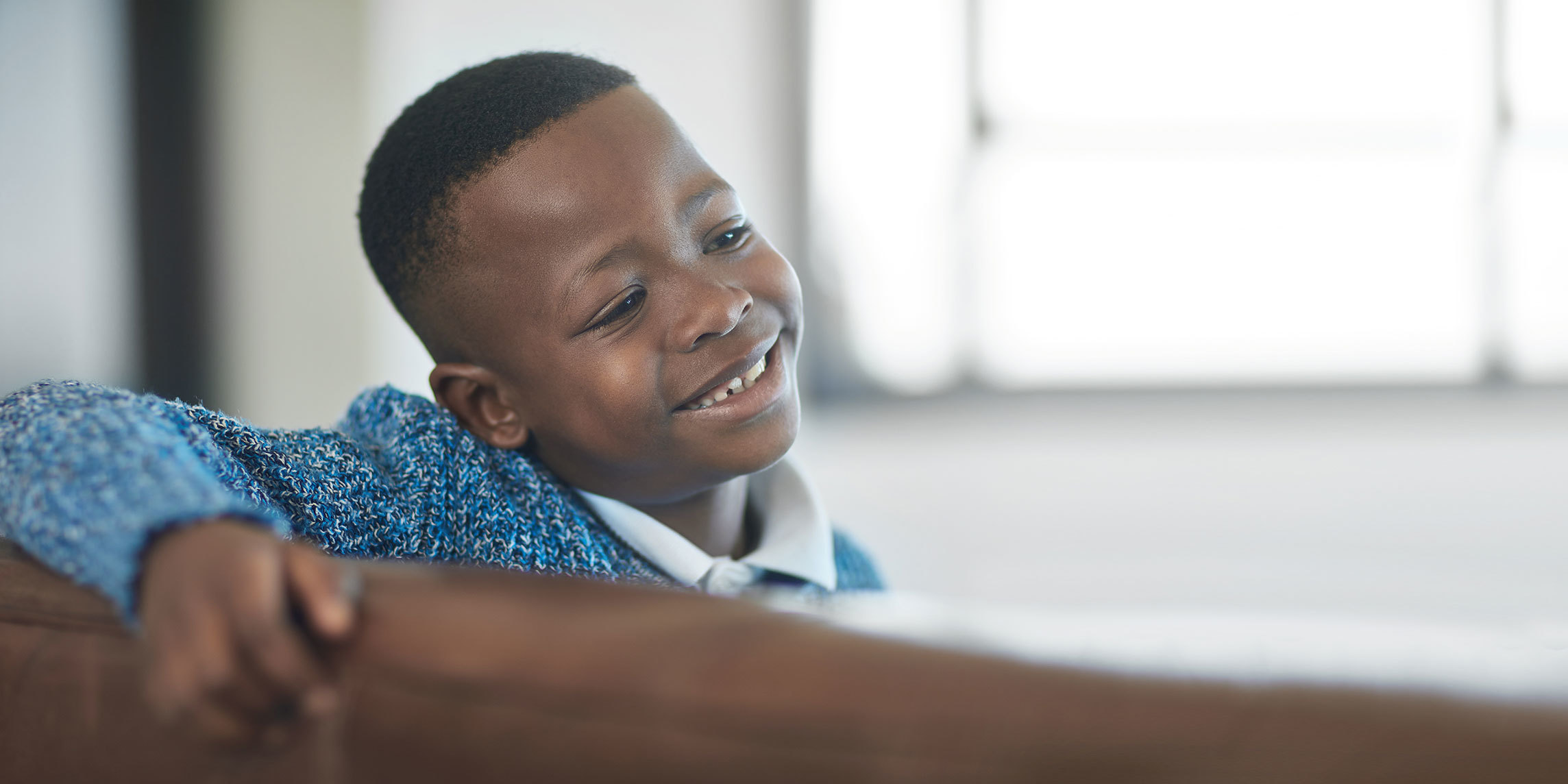 A young boy sitting and smiling on a wooden bench indoors.