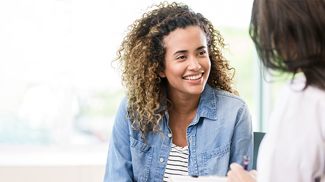 A young woman in a denim jacket smiling at a healthcare provider who is slightly out of frame.