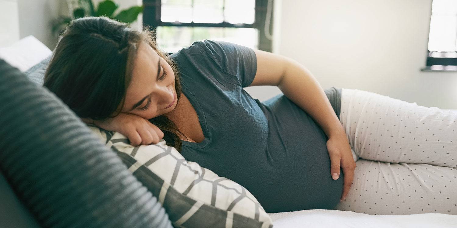 A pregnant woman lying on a couch and cradling her belly.