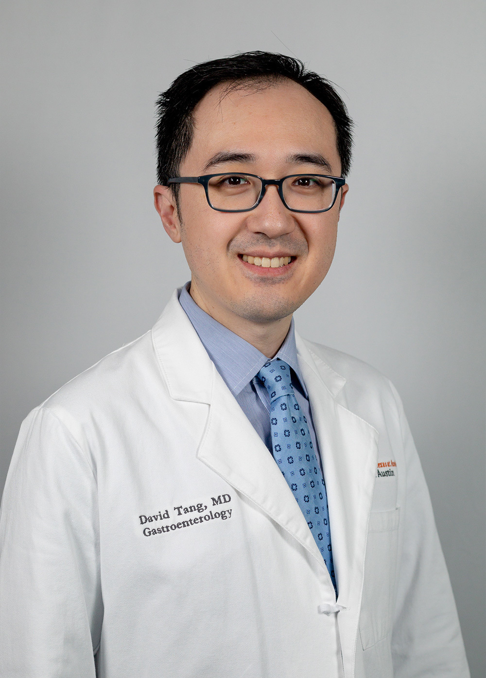 Dr. David Tang wearing a white coat and smiling in front of a white background.