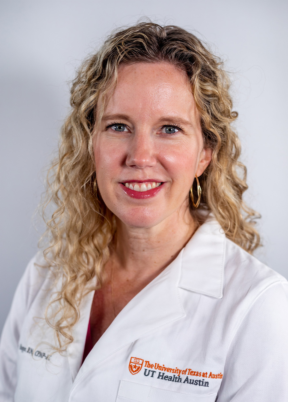 Emily Hopper wearing a white coat and smiling in front of a white backdrop.