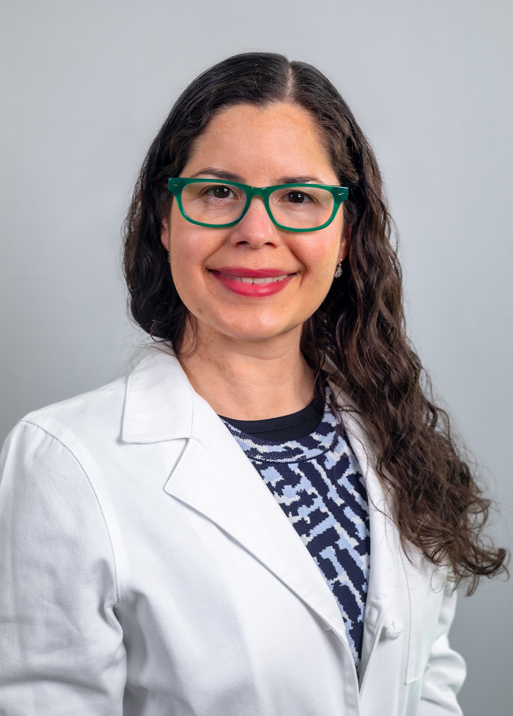 Physiatrist Glendaliz Bosques, MD, wearing a white coat and smiling in front of a white backdrop.