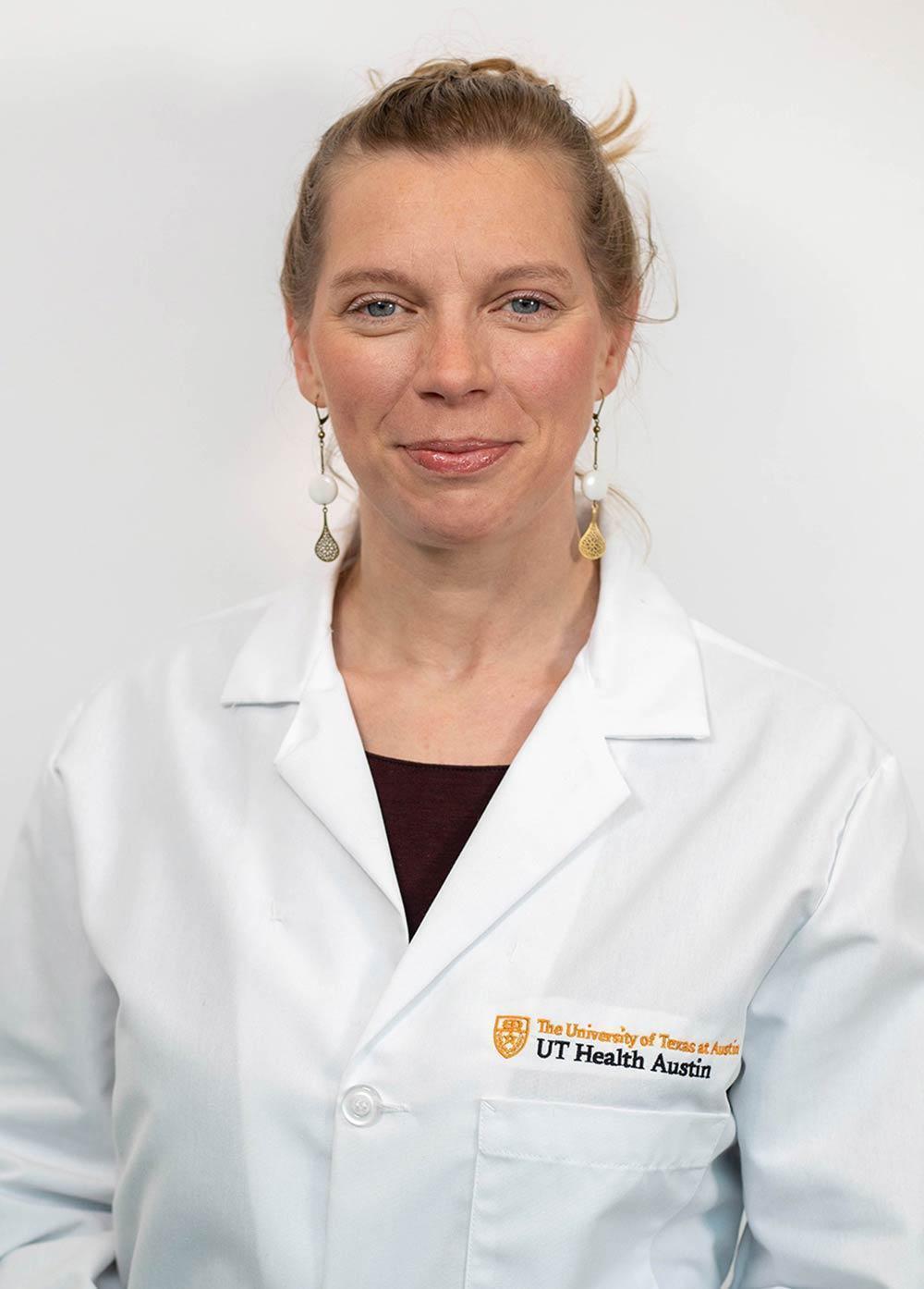 Dr. Kristina Jülich wearing a white coat and smiling in front of a white backdrop.