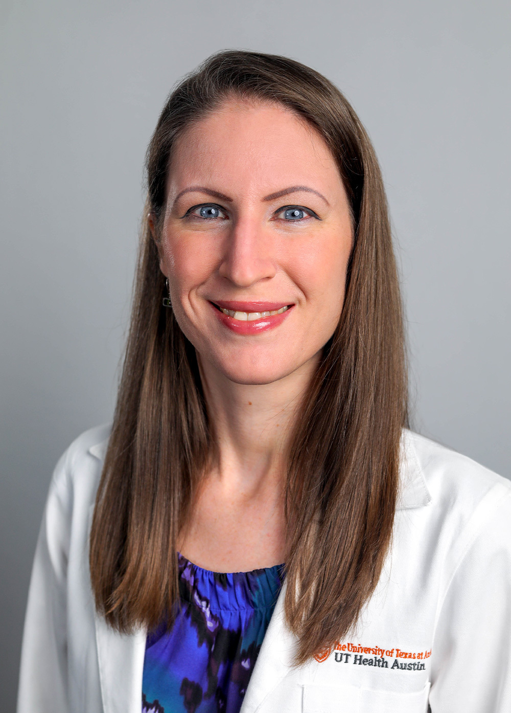 Katie Coleman wearing a white coat and smiling in front of a light gray backdrop.