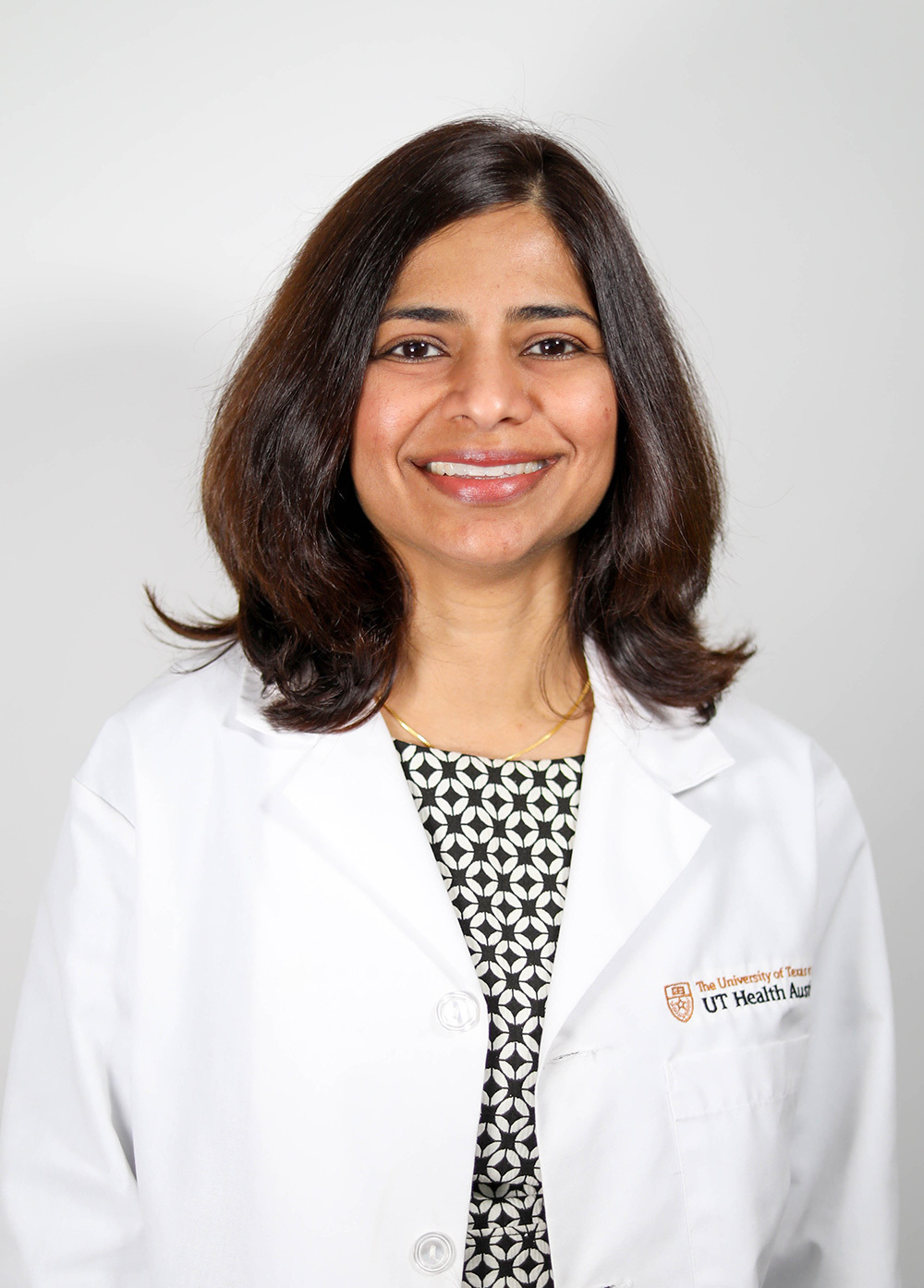 Dr. Kavitha Kumbum wearing a white coat and smiling in front of a white background.
