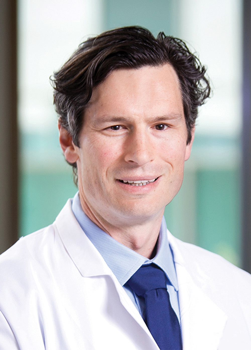 Dr. Kristopher M. Heinzman wearing a white coat and smiling indoors.