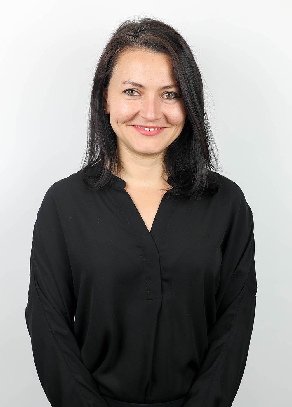 Lizette Taboada wearing a black blouse and smiling in front of a white backdrop.