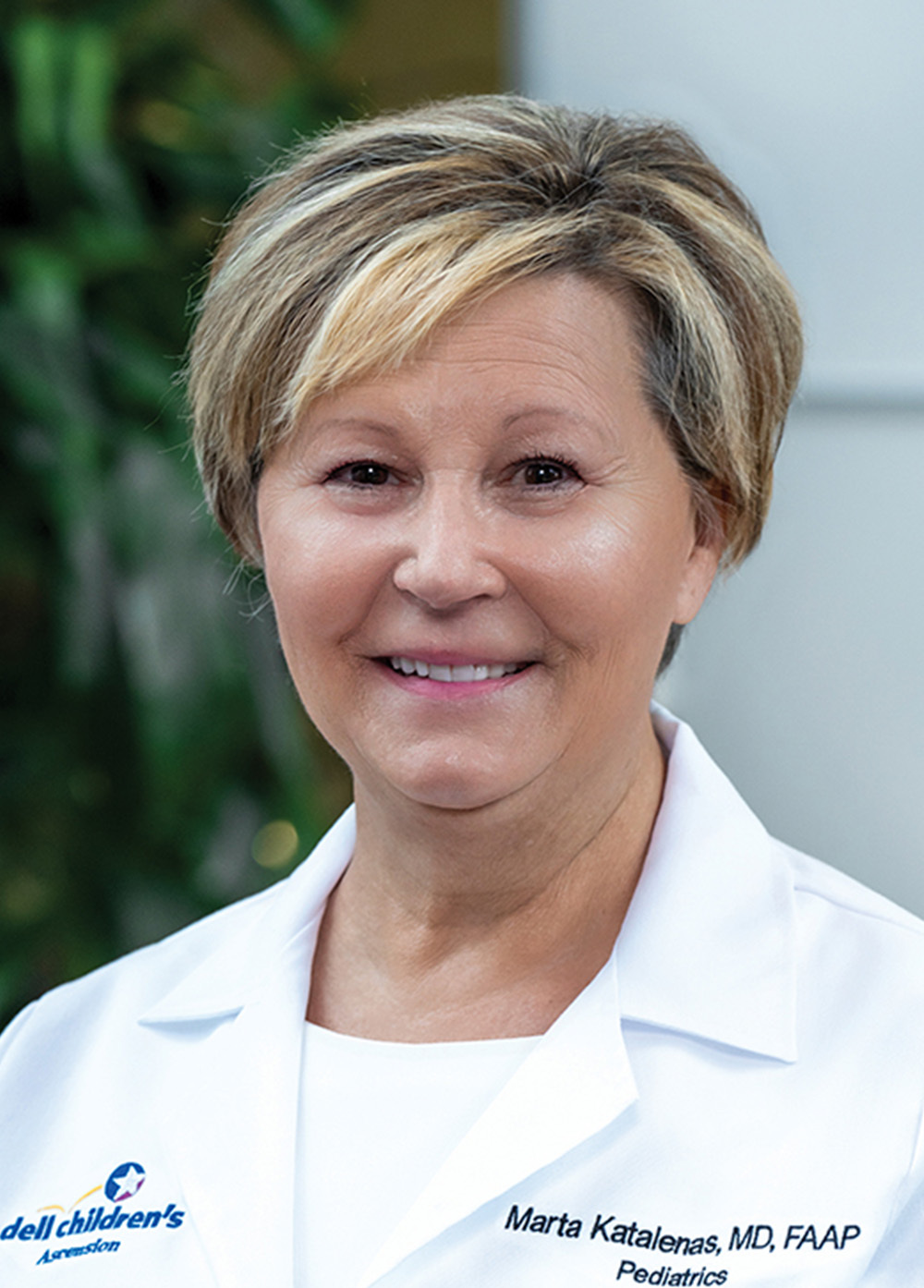 Pediatrician Marta Katalenas, MD, smiling and wearing a white coat with an embroidered Dell Children's Medical Center logo.