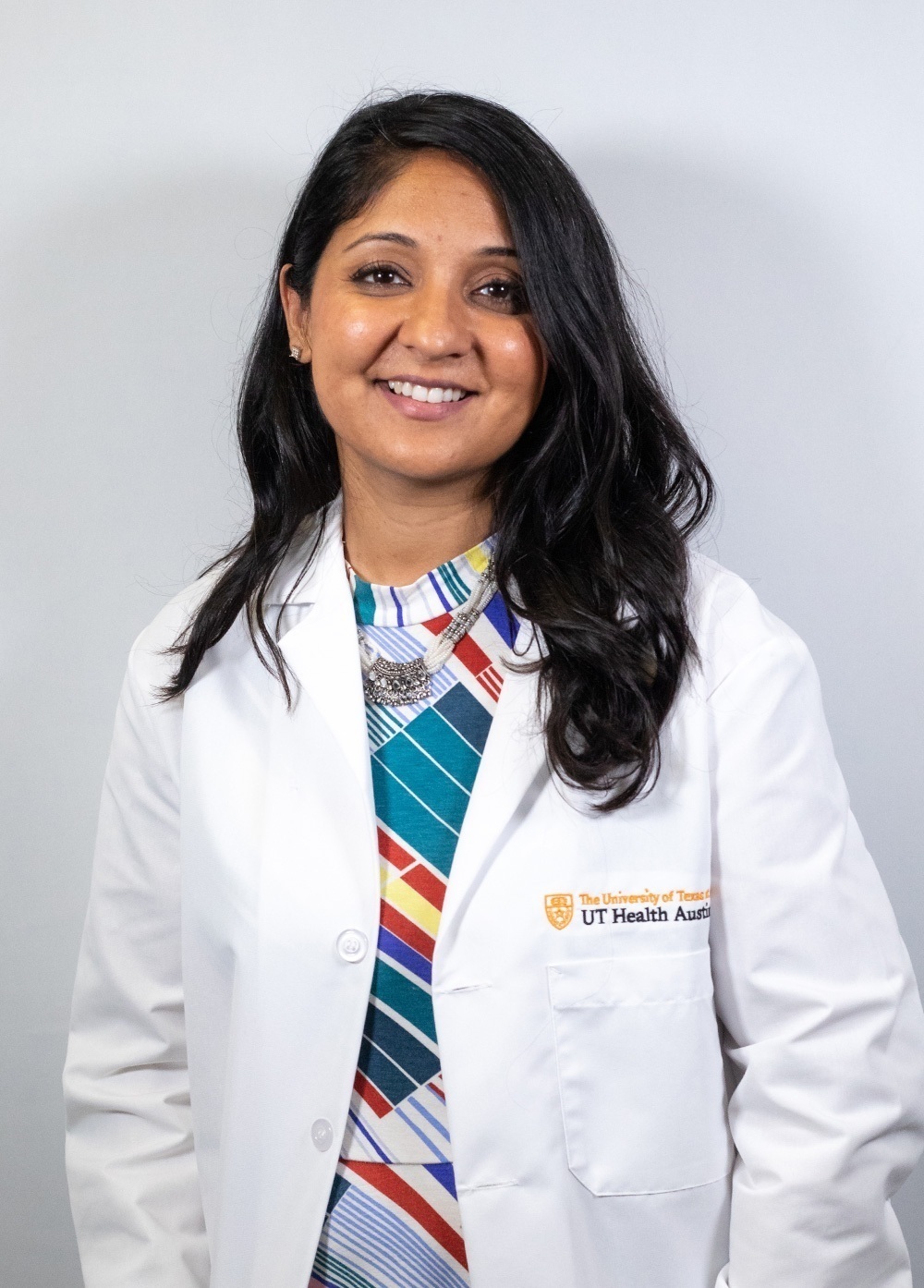 Dr. Puja G. Patel wearing a white coat and smiling in front of a white backdrop.