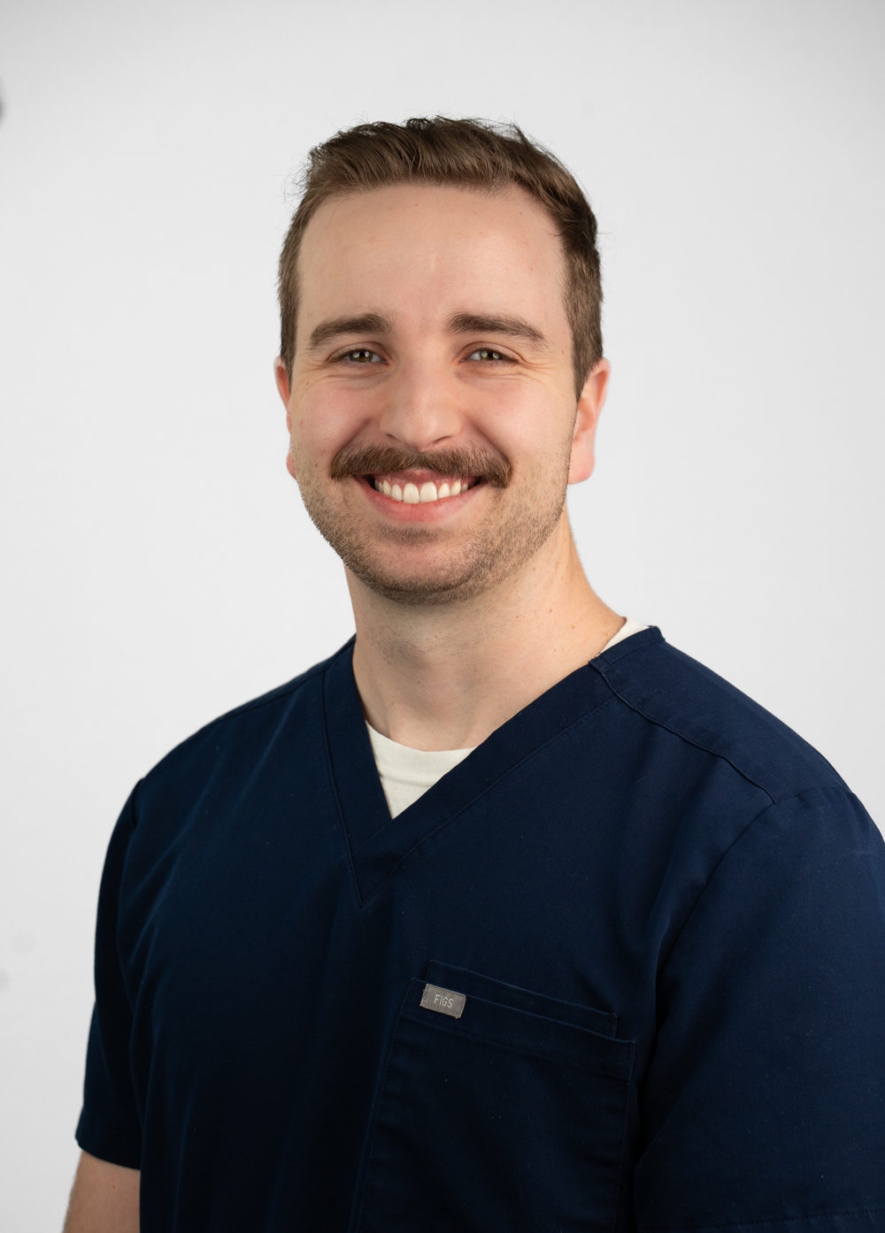Headshot of Sam Manselle. He is wearing dark navy blue scrubs.
