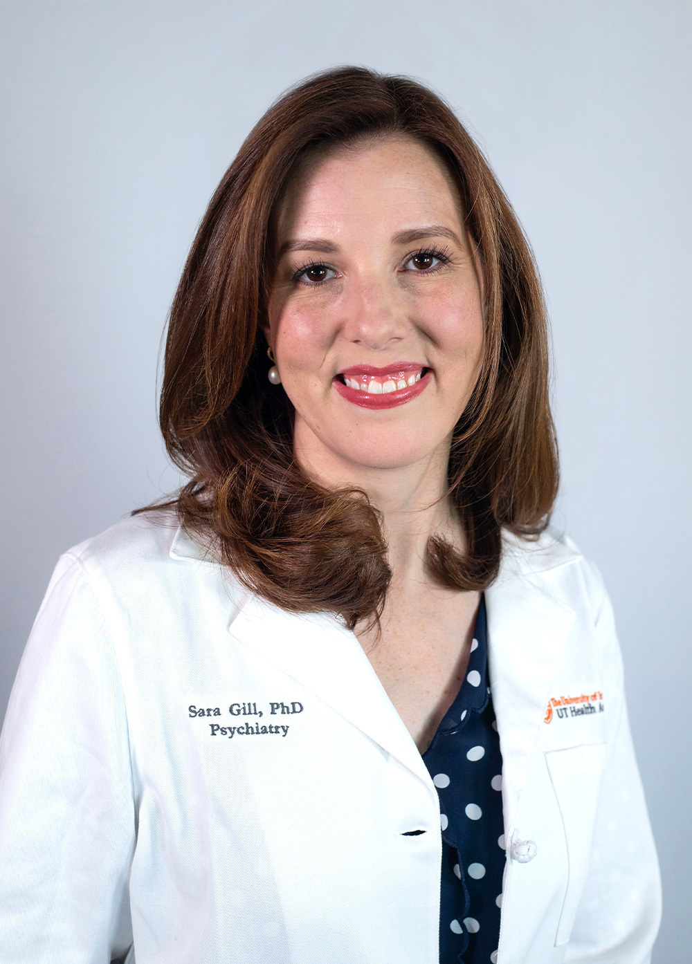 Dr. Sara Gill wearing a white coat and smiling in front of a white backdrop.