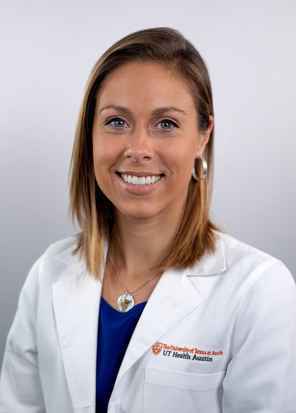 Dr. Sarah Schofstall wearing a white coat and smiling in front of a white backdrop.