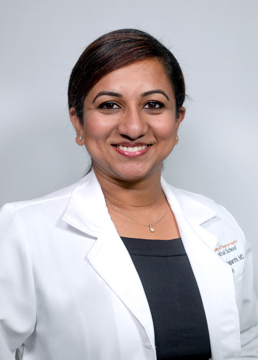 Dr. Sireesha Chinthaparthi wearing a white coat and smiling in front of a white backdrop.