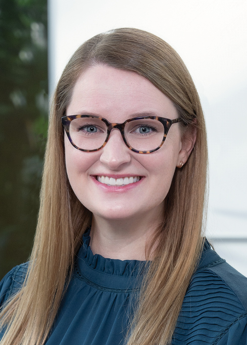 Pediatric Headache Program Coordinator Zoë Allen, MBA, BSN, RN, smiling in a teal blouse and glasses. She has light brown hair.