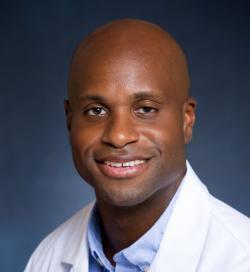 Dr. Kobina Ghartey wearing a white coat and smiling in front of a dark blue backdrop.
