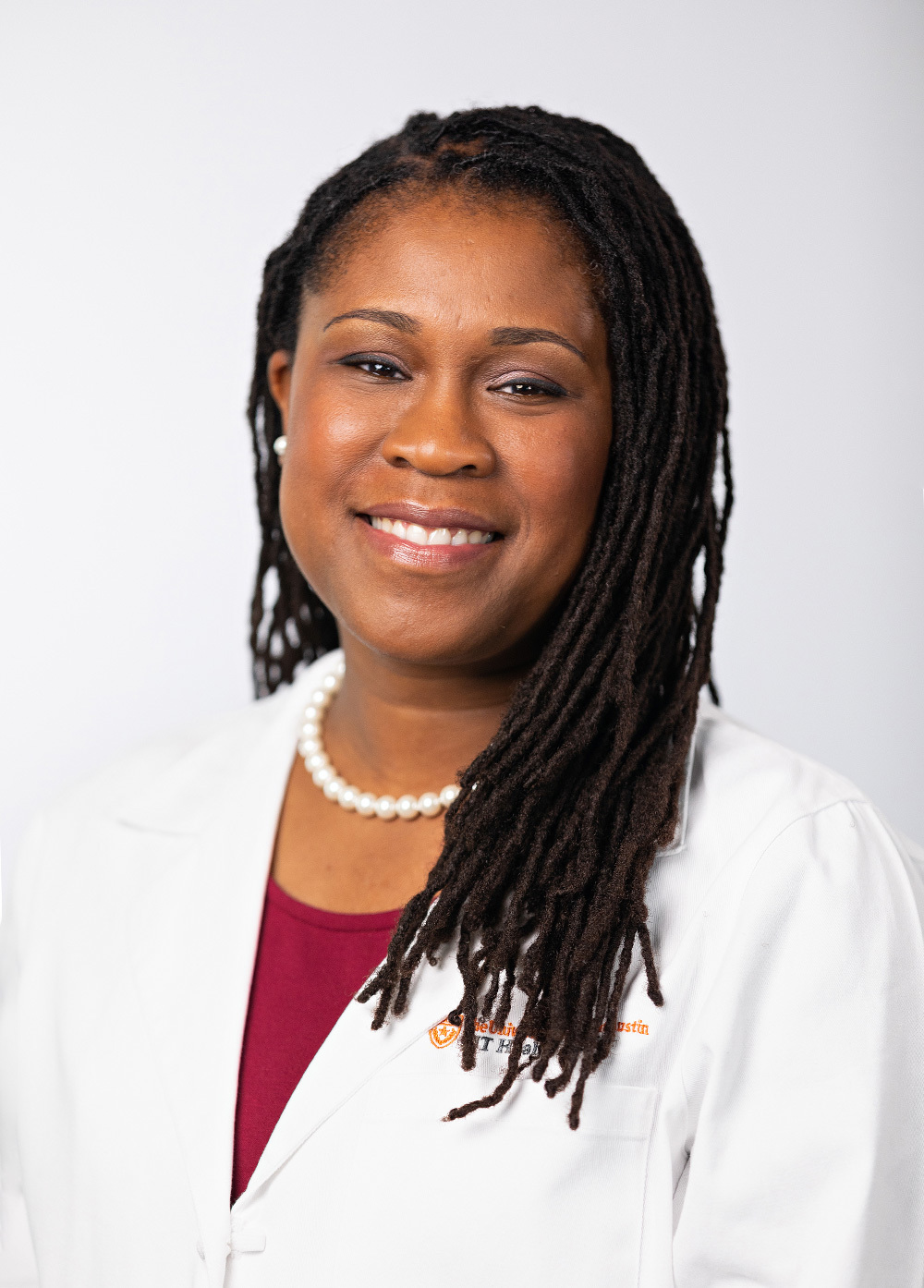 Dr. Akua Afriyie-Gray wearing a white coat and smiling in front of a white backdrop.
