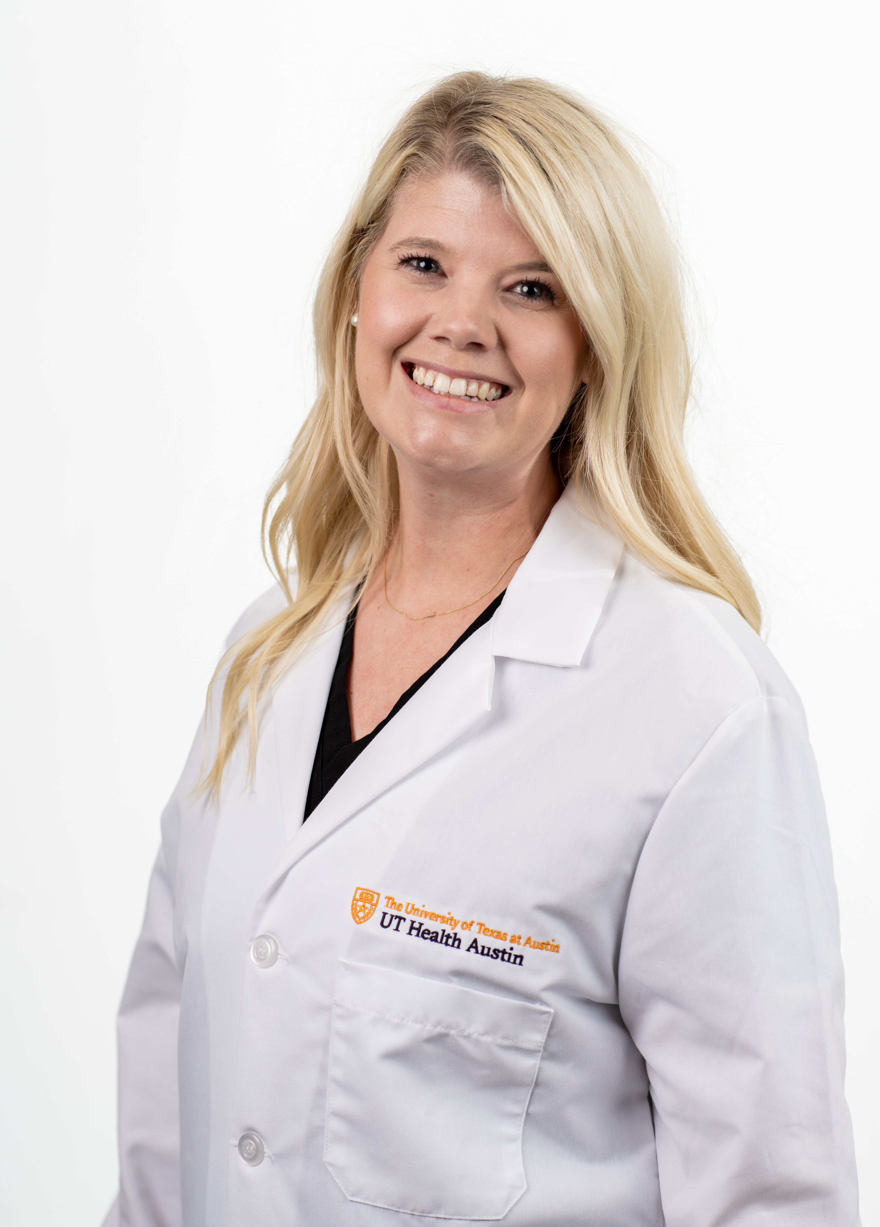 Acute care pediatric nurse practitioner Amber Matthews, MSN, APRN, CPNP-AC smiling in front of a white backdrop. She is wearing a white coat with an embroidered UT Health Austin logo.