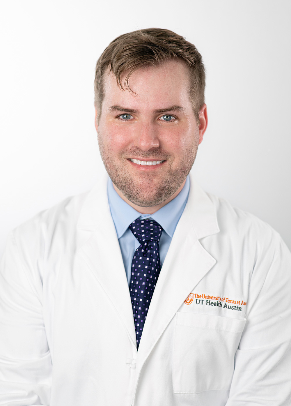 Dr. Austin Adair wearing a white coat and smiling in front of a white backdrop.