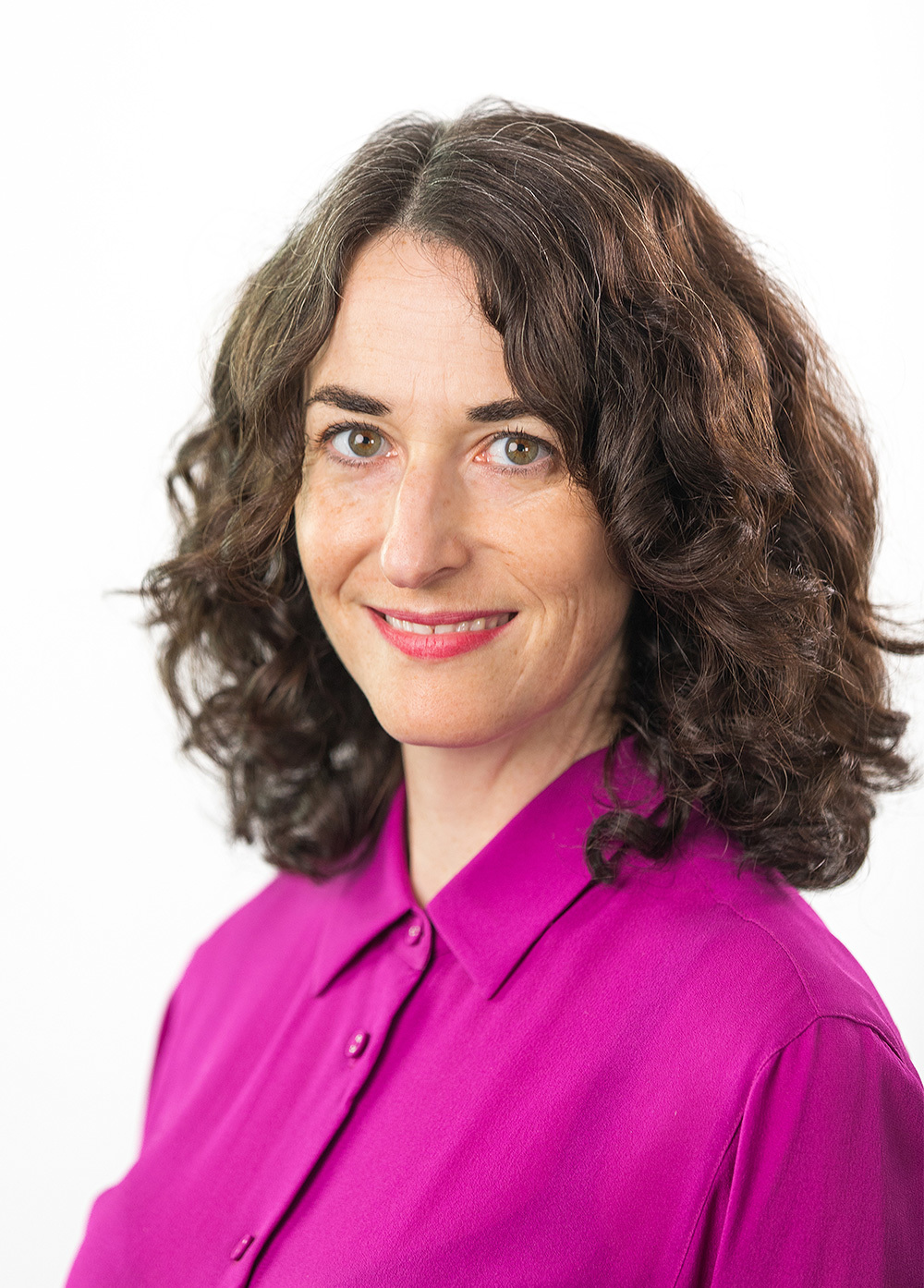 Clarissa Colley wearing a pink blouse and smiling in front of a white backdrop.