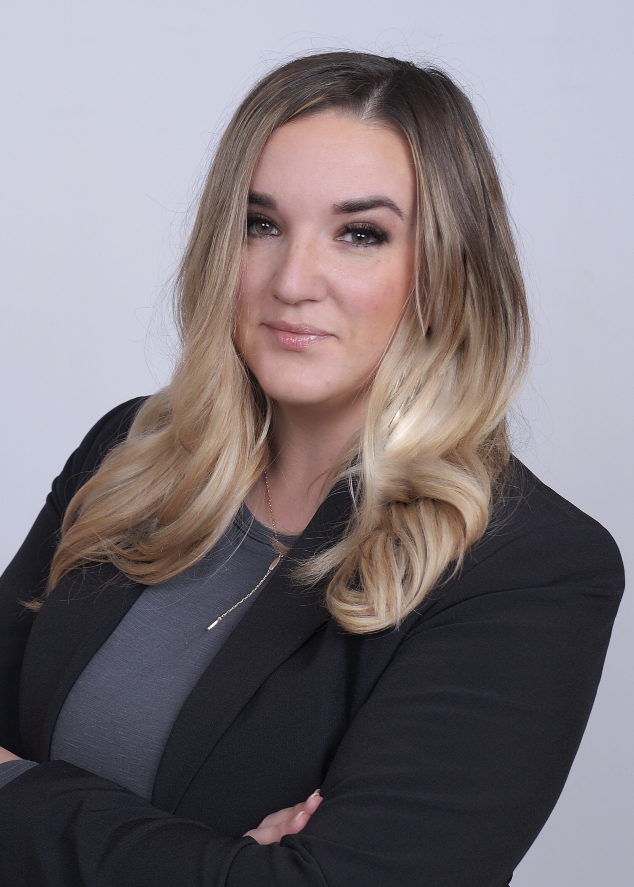 Danielle Bruns wearing gray shirt and black blazer and smiling in front of a white backdrop.
