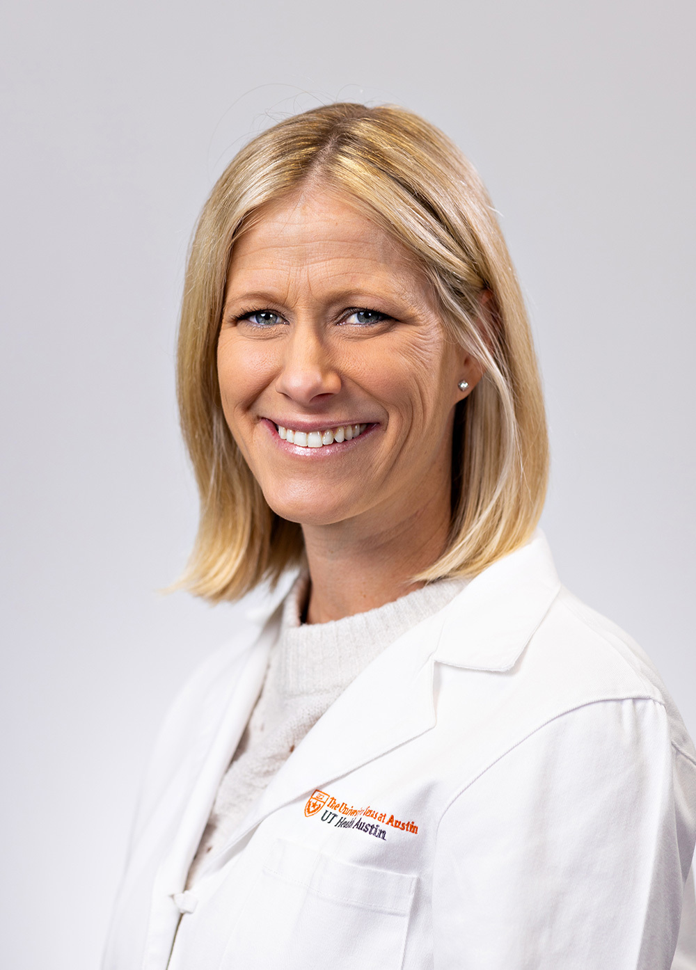 Elizabeth McBrearty wearing a white coat and smiling in front of a white backdrop.