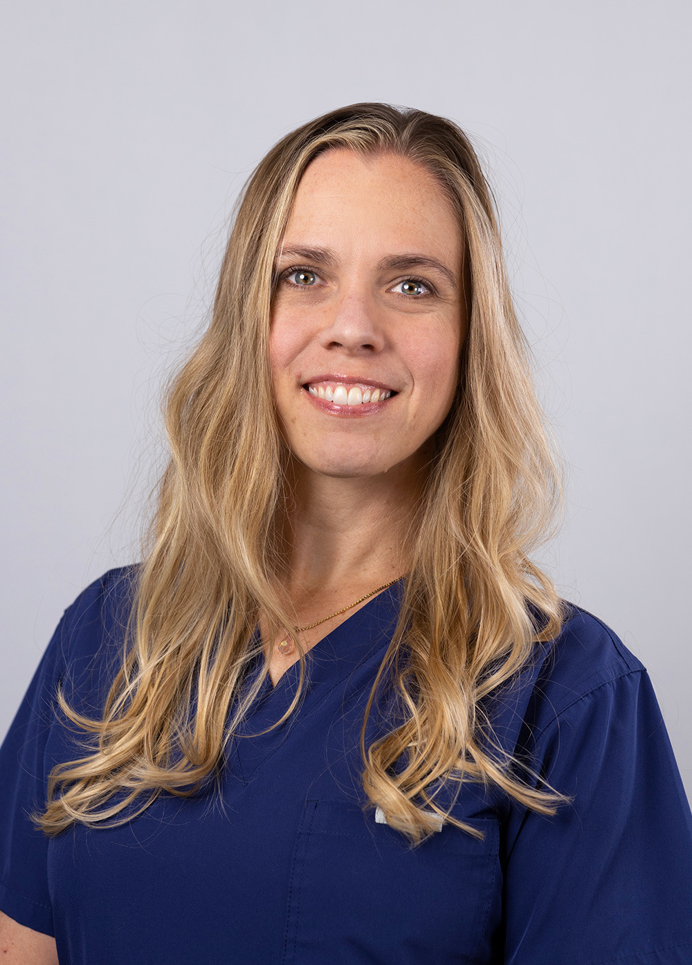 Emily Hutson wearing navy scrubs and smiling in front of a white backdrop.