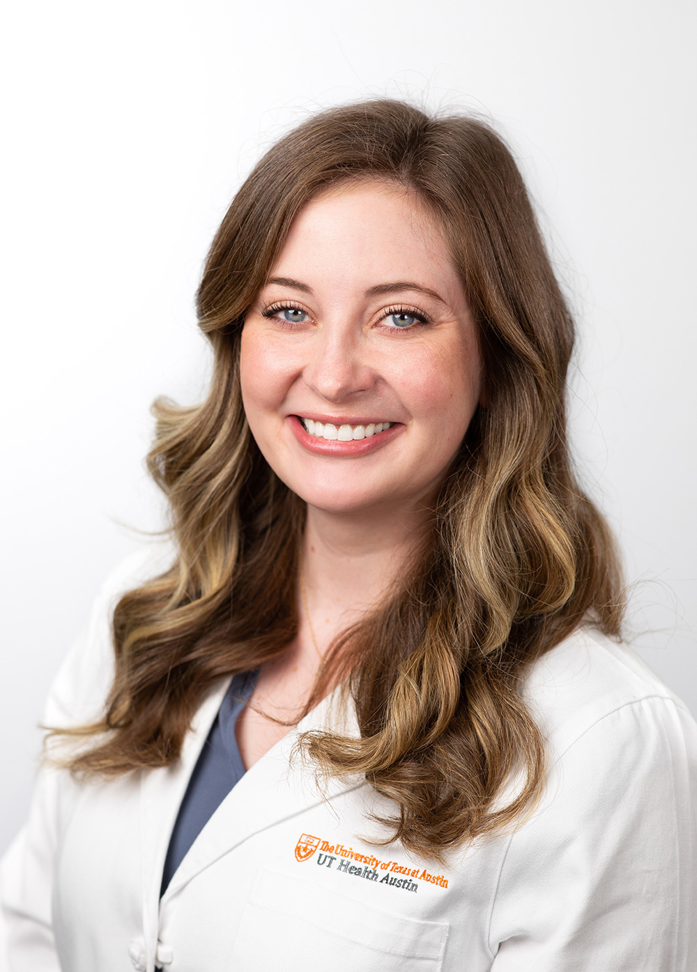 Erin Moise wearing a white coat and smiling in front of a white background.