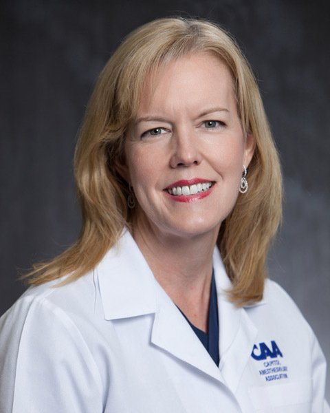 Holly Gunn wearing a white coat and smiling in front of a gray background.