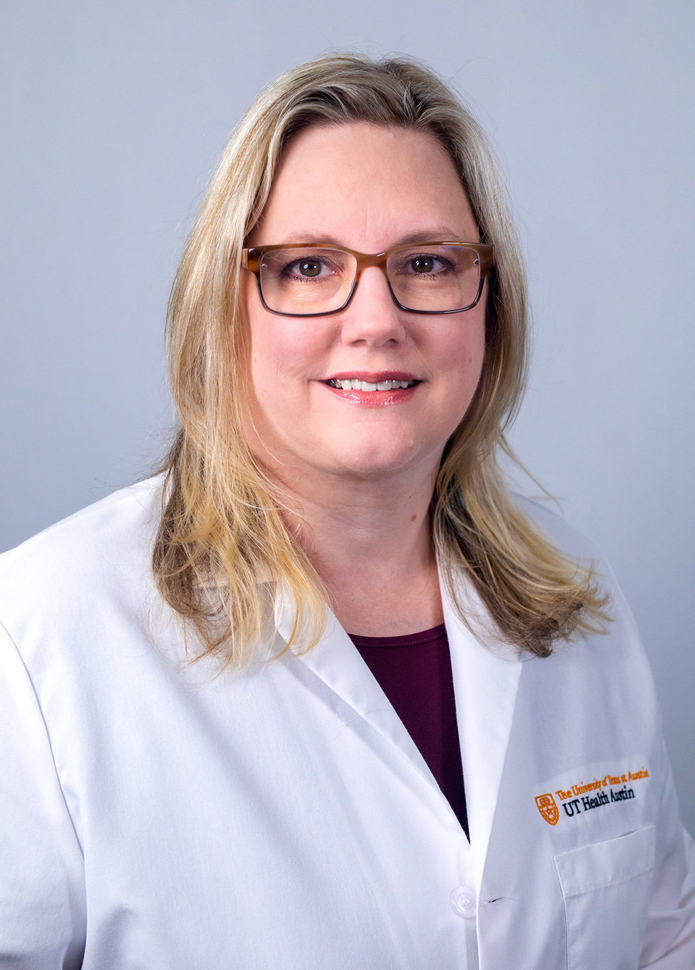 Jena Hiltenbrand wearing a white coat and smiling in front of a white backdrop.