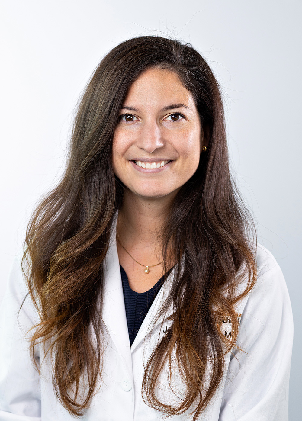 Dr. Jenny Travieso wearing a white coat and smiling in front of a white background.