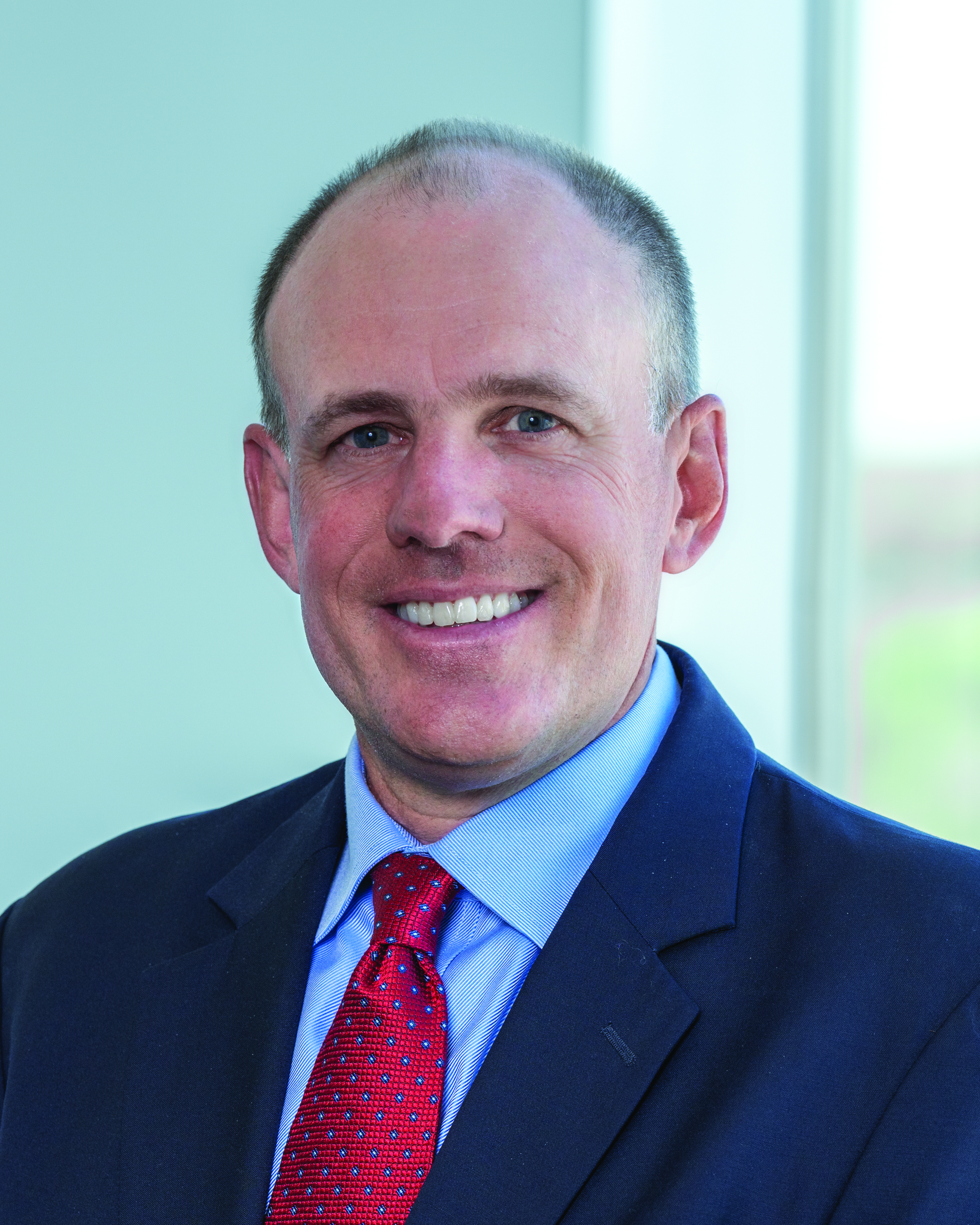 Dr. John Harkins wearing suit and tie and smiling near a window.