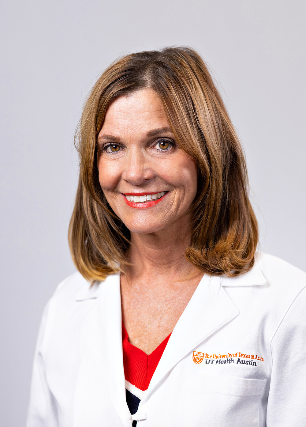 Joni Zauhar wearing a white coat and smiling in front of a white backdrop.