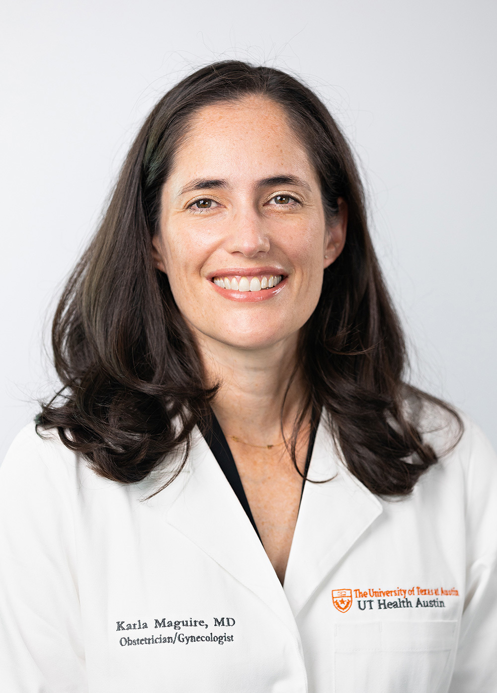 Dr. Karla Maguire wearing a white coat and smiling in front of a white backdrop.