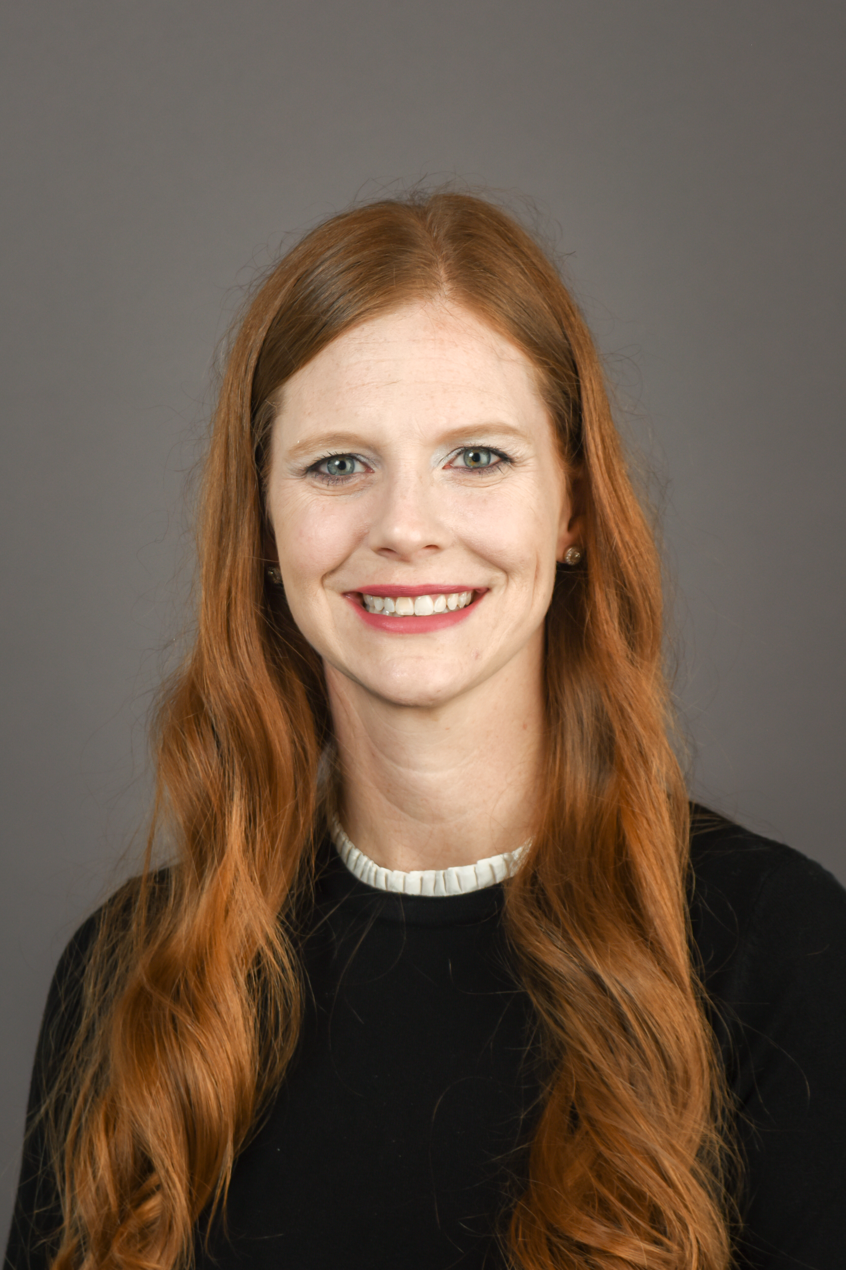 Dr. Katherine Kohls wearing a black shirt and smiling in front of a gray backdrop.