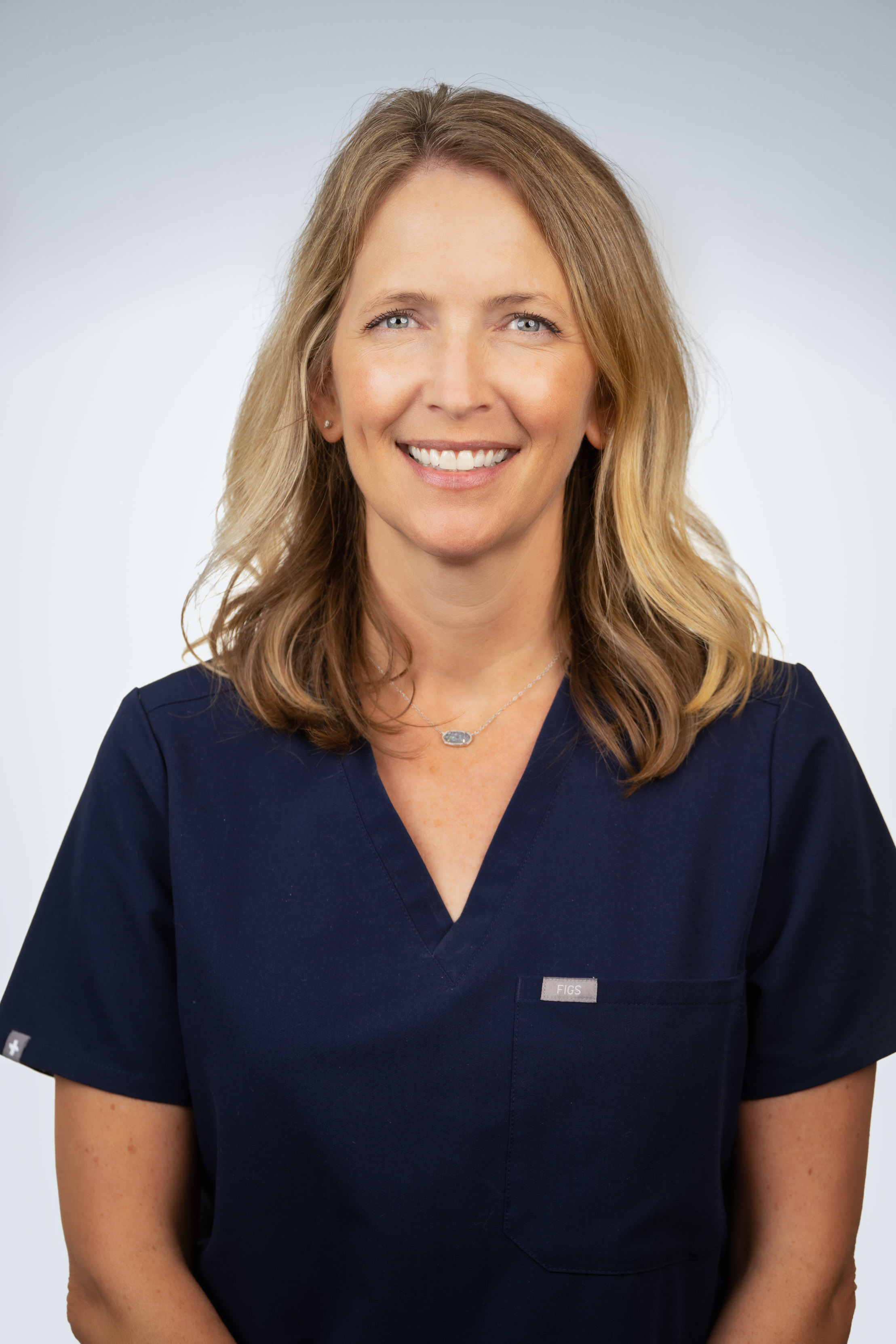 Kelli Andrews wearing dark scrubs and smiling in front of a white backdrop.