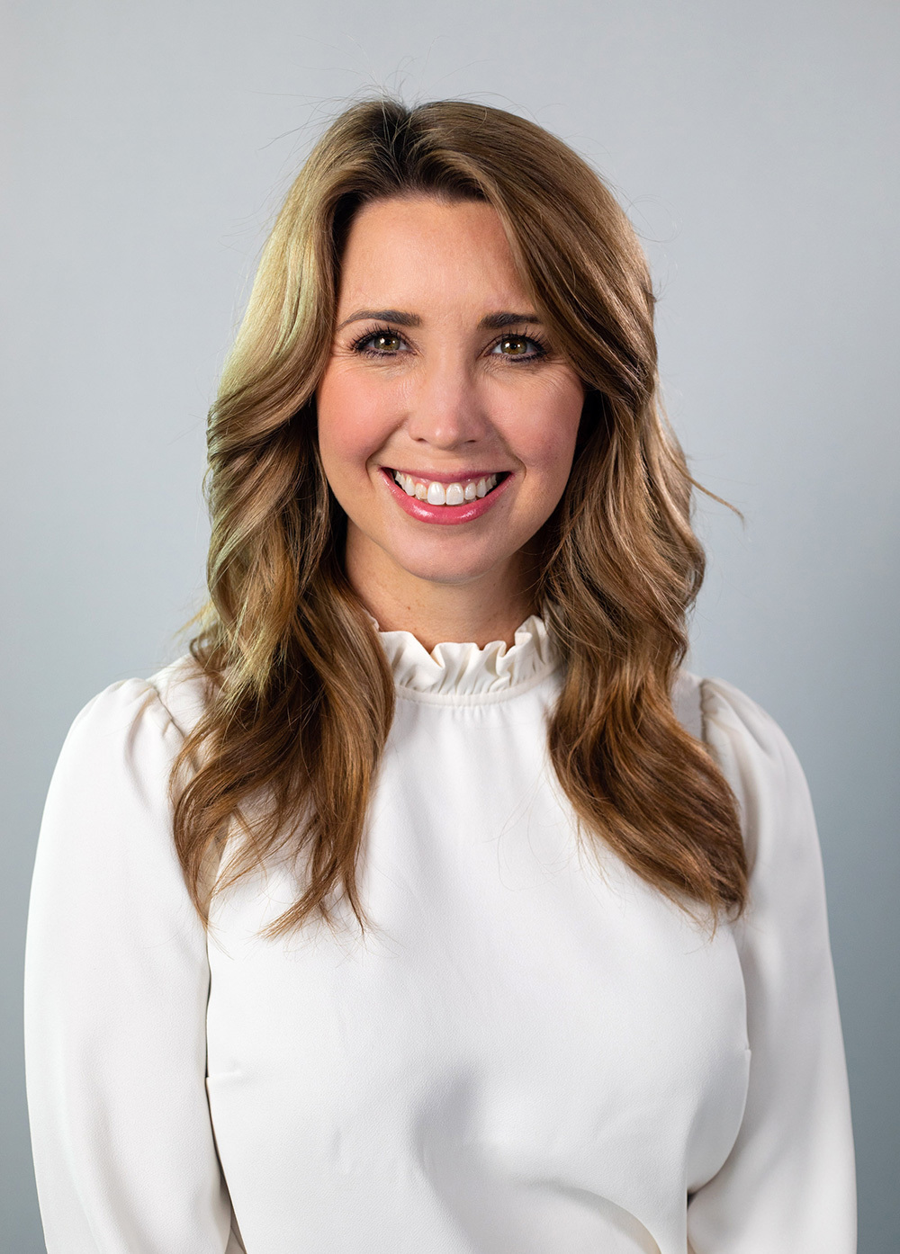 Krystle Pleitz wearing a white blouse and smiling in front of a white background.