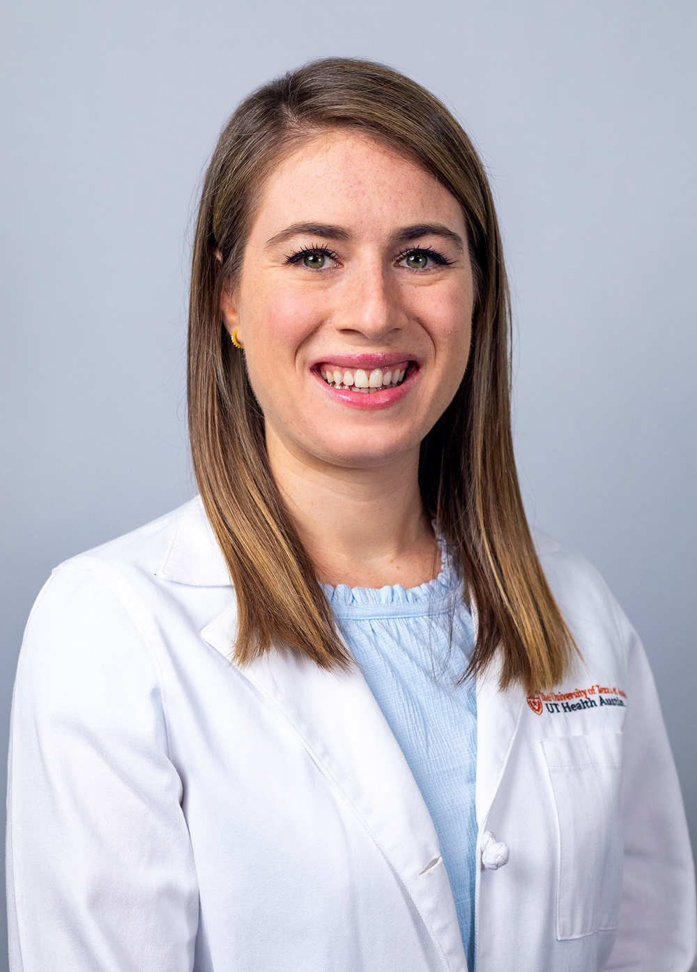Laura Kerr wearing a white coat and smiling in front of a white backdrop.