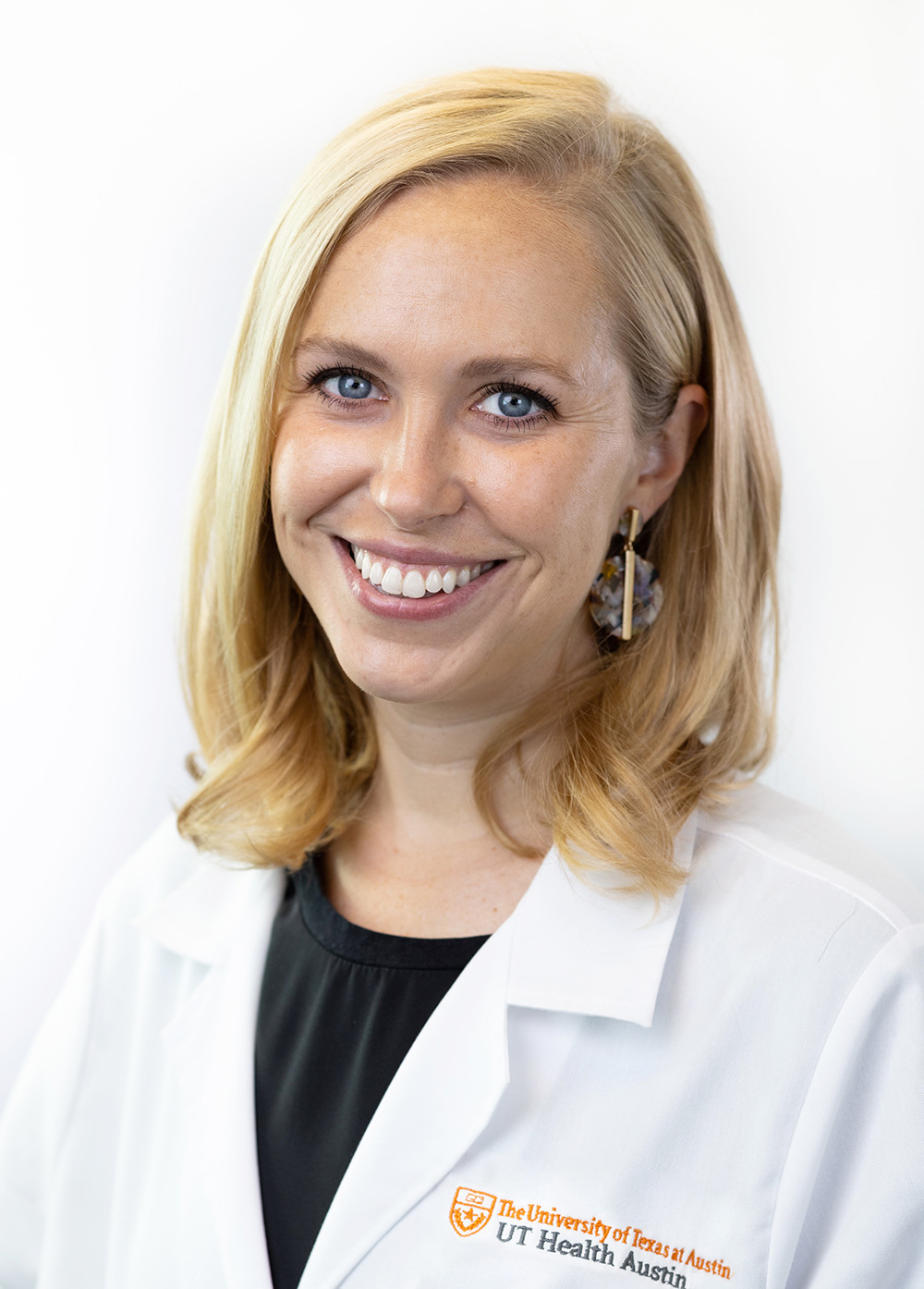 Dr. Mary Rieger wearing a white coat and smiling in front of a white backdrop.