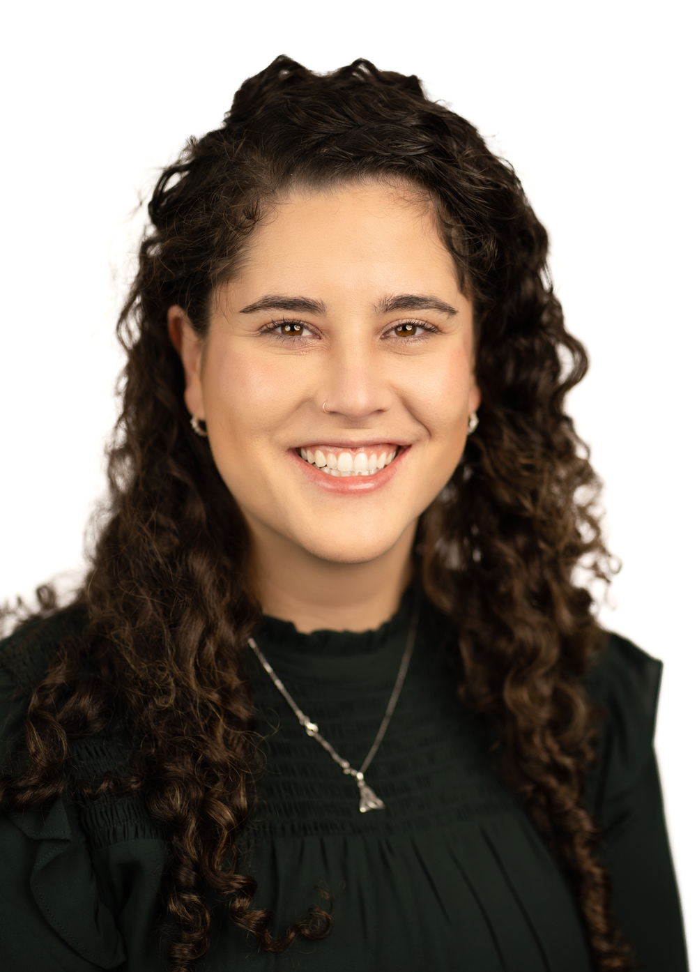 Mayajoy Sheridan wearing a black blouse and smiling in front of a white backdrop.