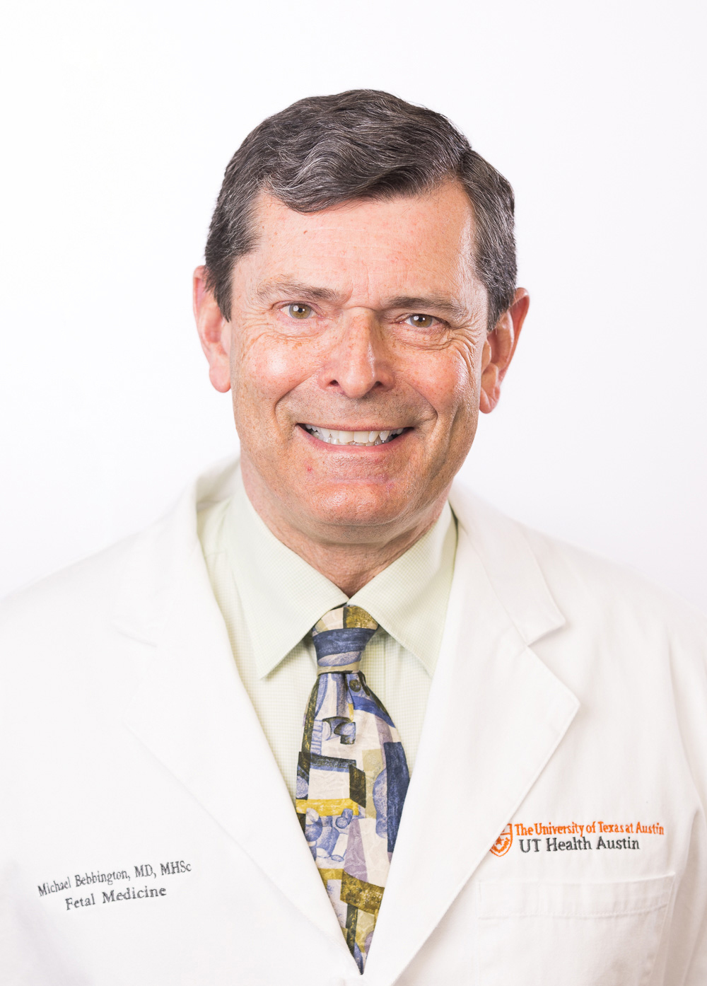 Dr. Michael Bebbington wearing a white coat and smiling in front of a white backdrop.