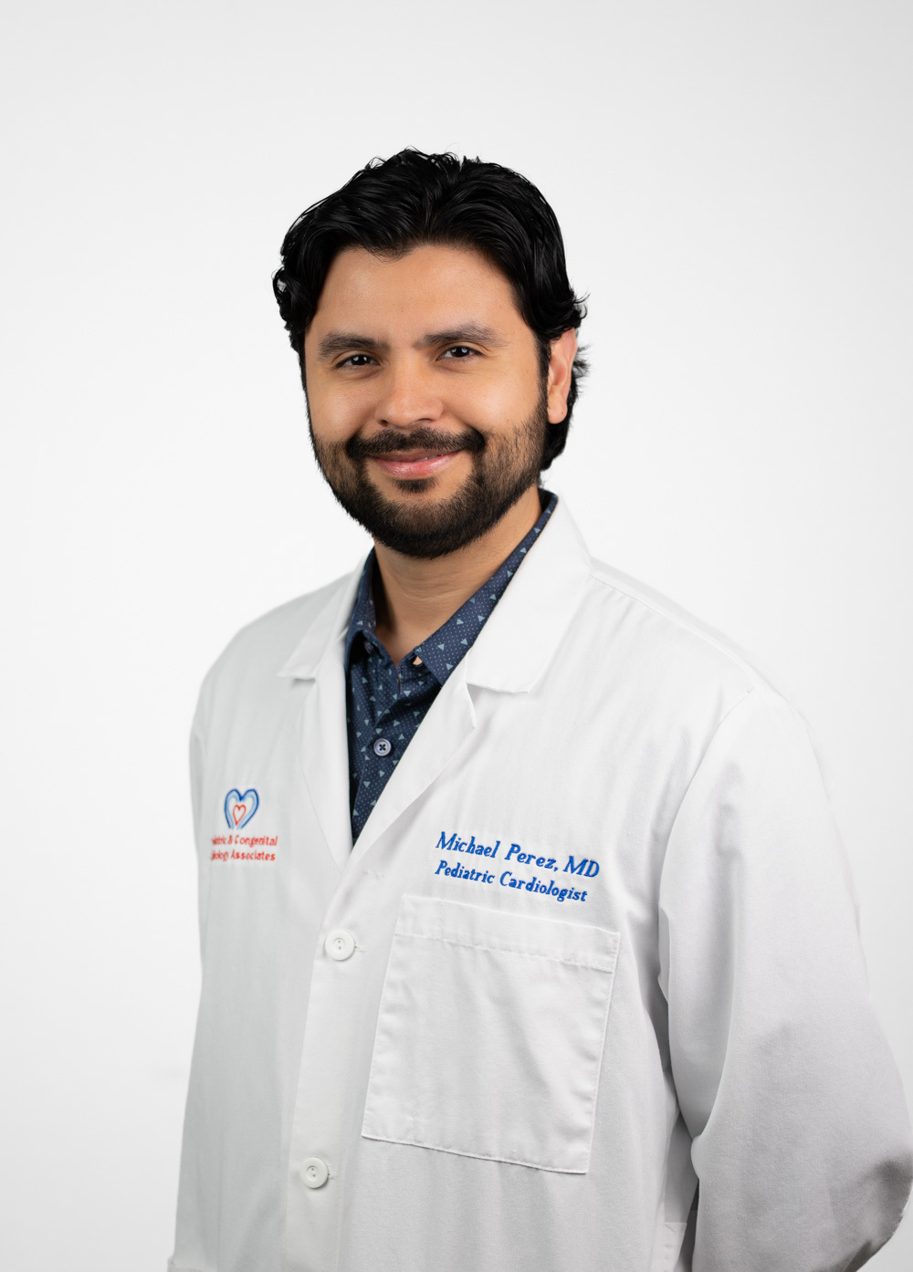 Dr. Perez is looking at the camera and smiling. He is wearing a white coat with a blue dress shirt.