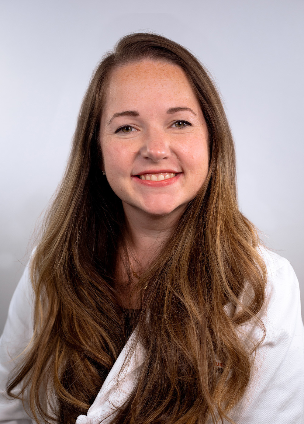 Michelle McCartney wearing a white coat and smiling in front of a white backdrop.