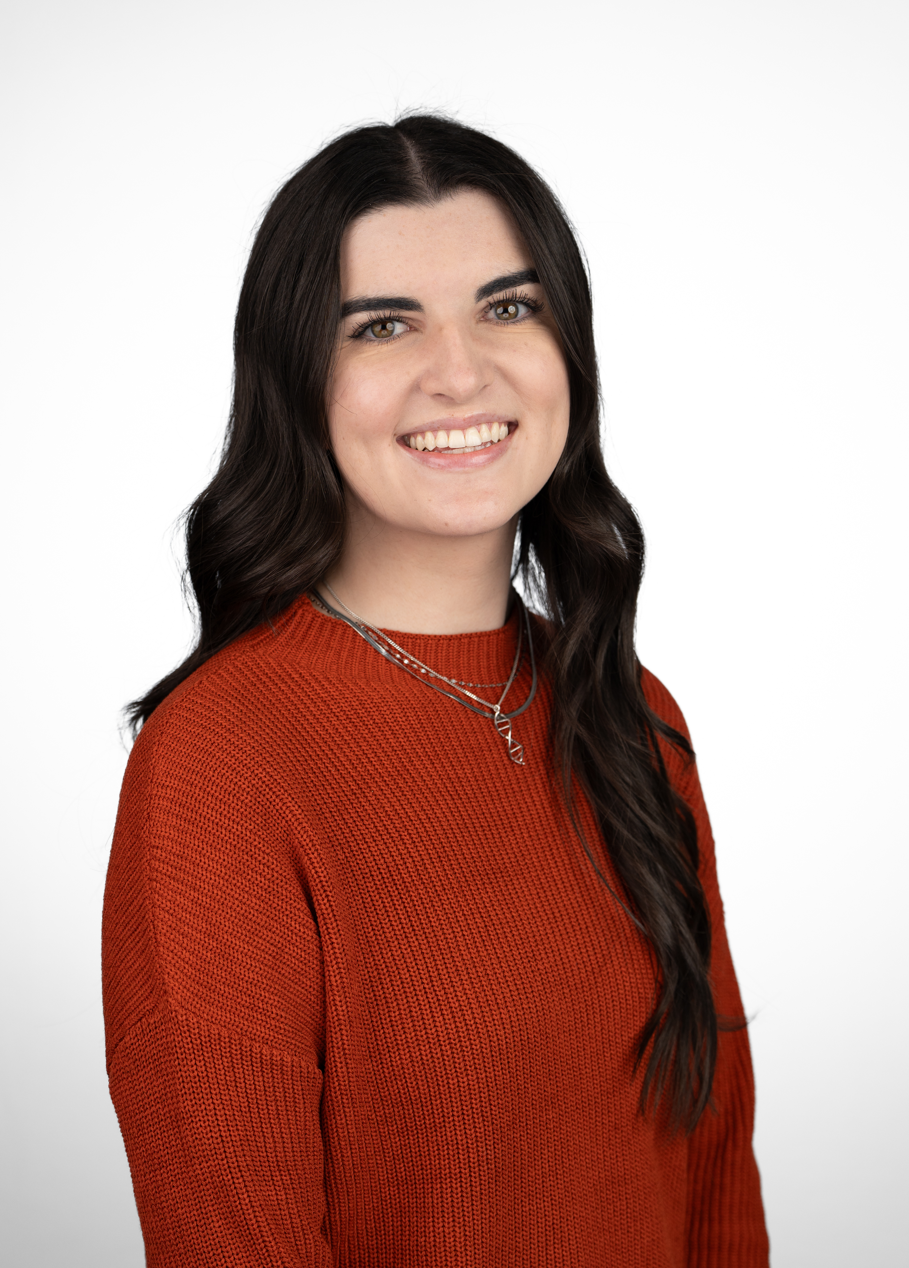 Genetic counselor Olivia Roy, MS, CGC, wearing a red-orange sweater and smiling in front of a white backdrop.