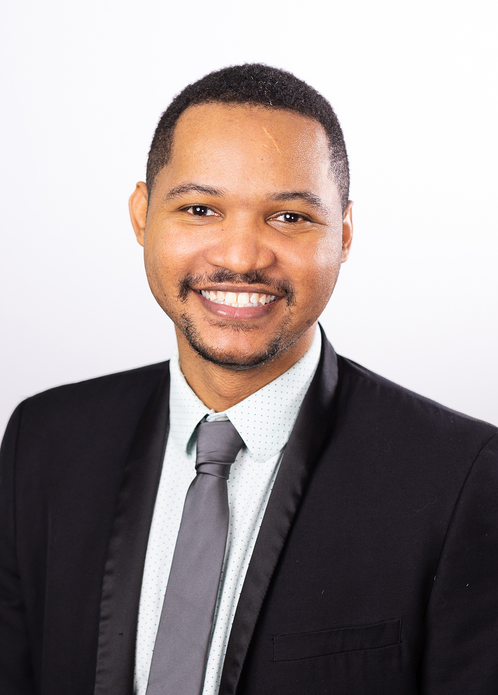 Patrick Woodson wearing a suit and gray tie and smiling in front of a white backdrop.