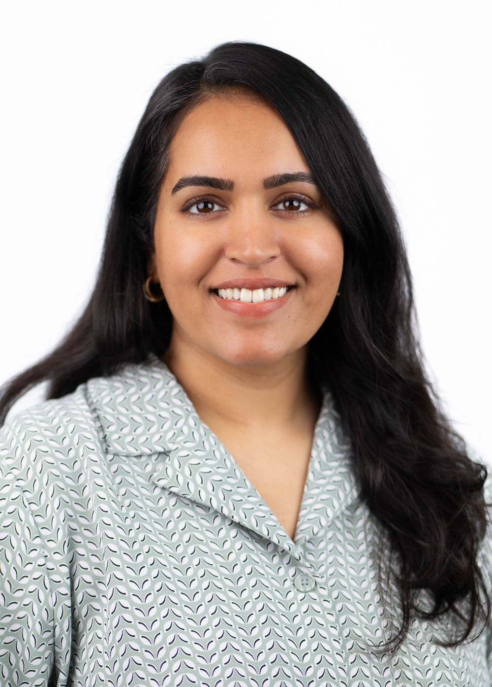 Rachana Varghese is looking at the camera and smiling. She is wearing a white and mint green patterned blouse.