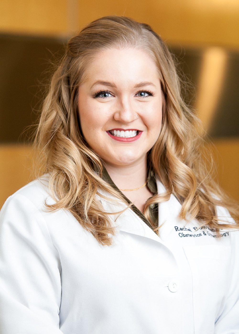 Obstetrician-gynecologist Rachel Bowman, MD, wearing a white coat and smiling indoors.