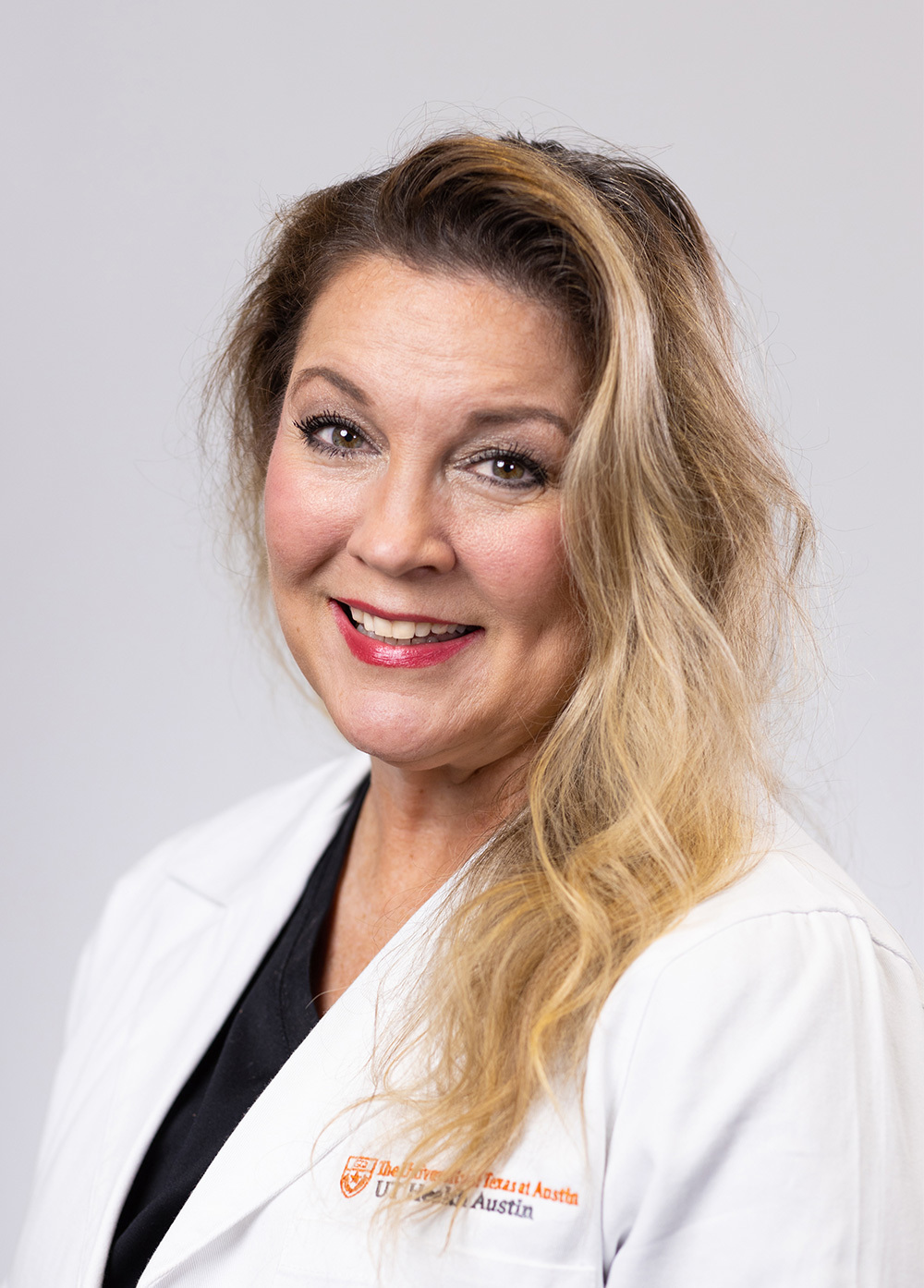Rebecca Byars wearing a white coat and smiling in front of a white backdrop.
