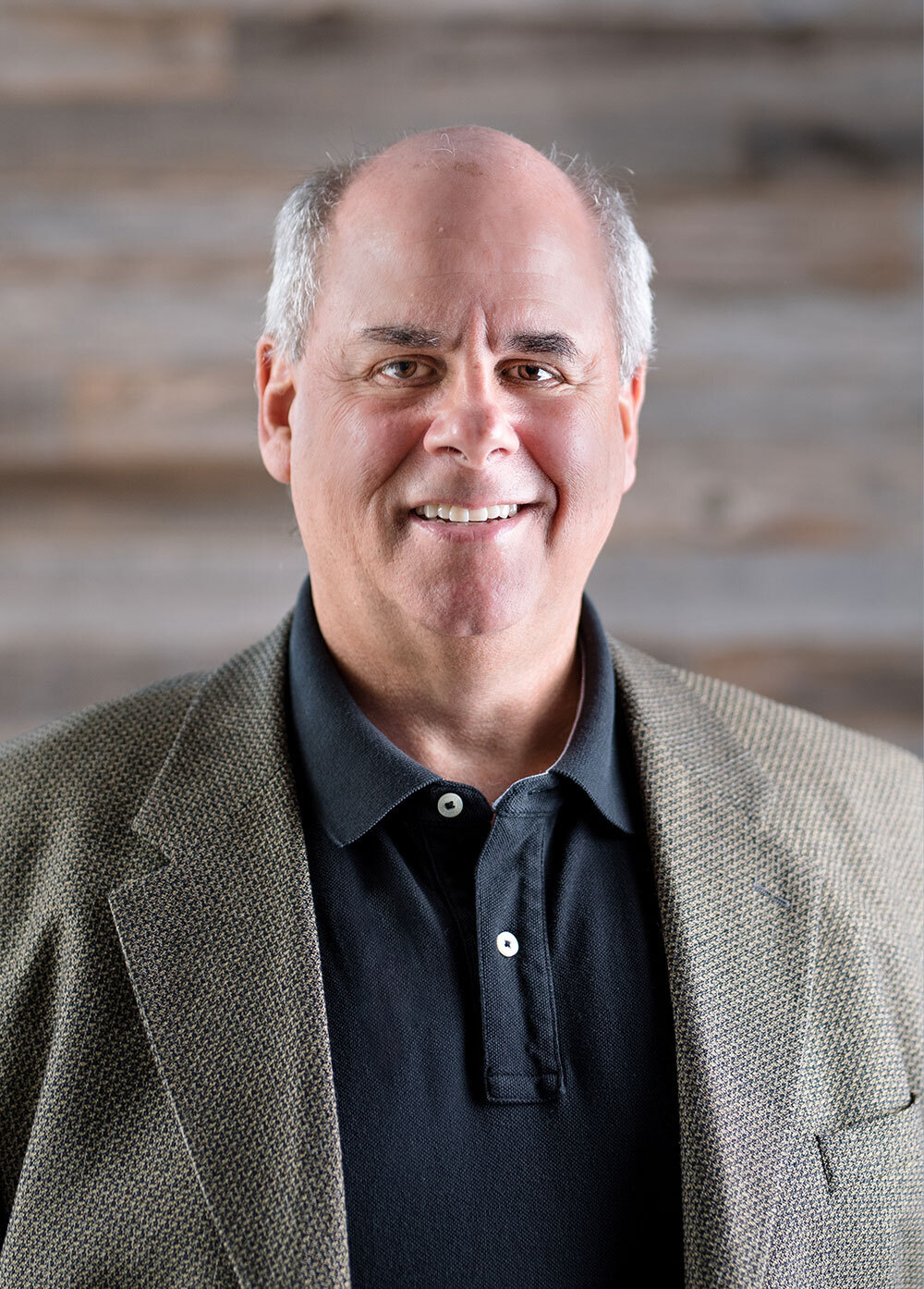 Pediatric cardiologist and consulting clinician Ron Shapiro, MD, smiling in front of a wooden wall. He is wearing a navy collared shirt and gray jacket.